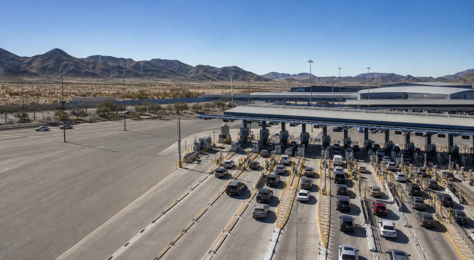 Passenger vehicles moving through border inspection lanes under clear skies.