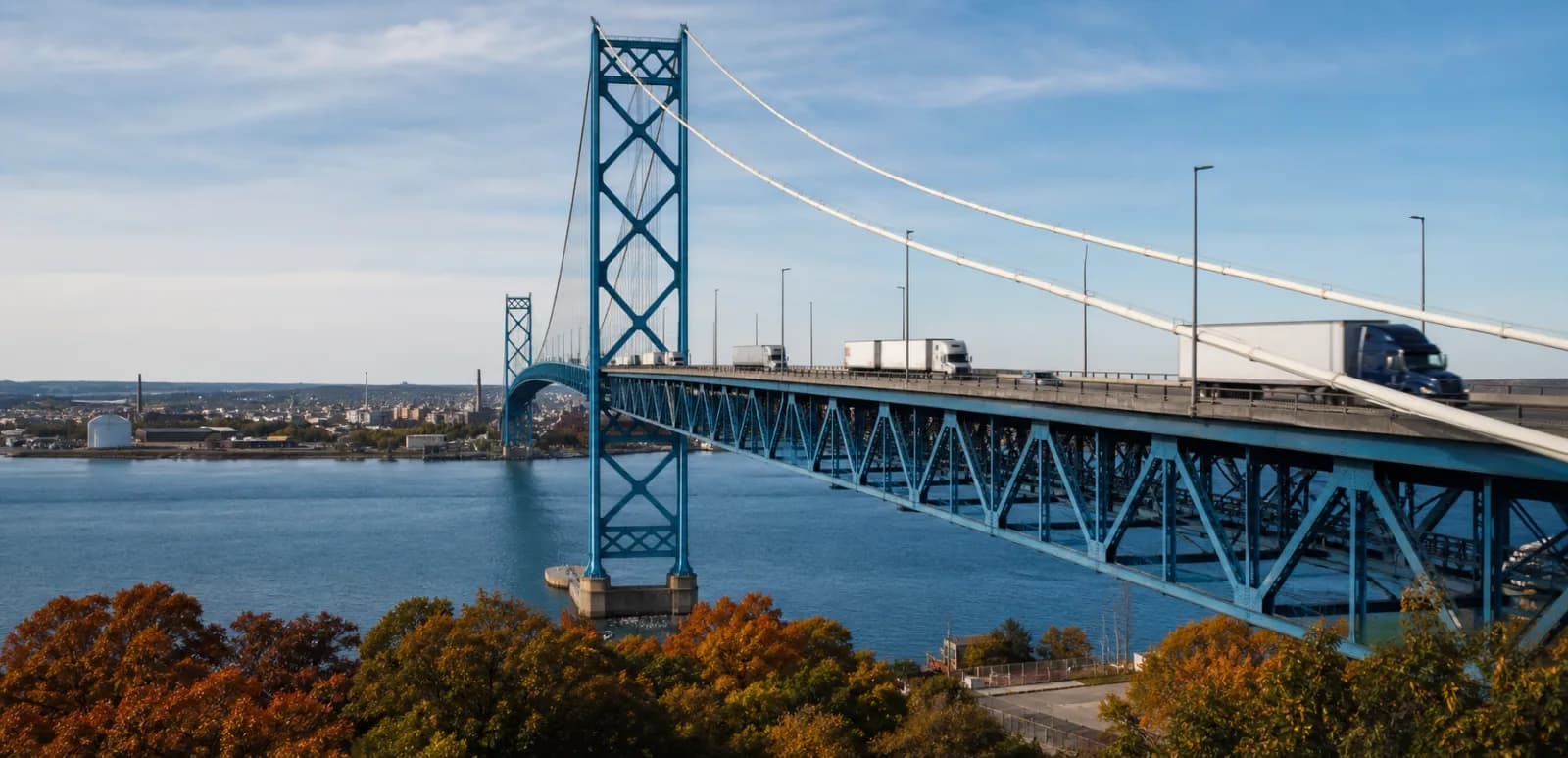 Commercial trucks traveling across a large bridge above blue water.