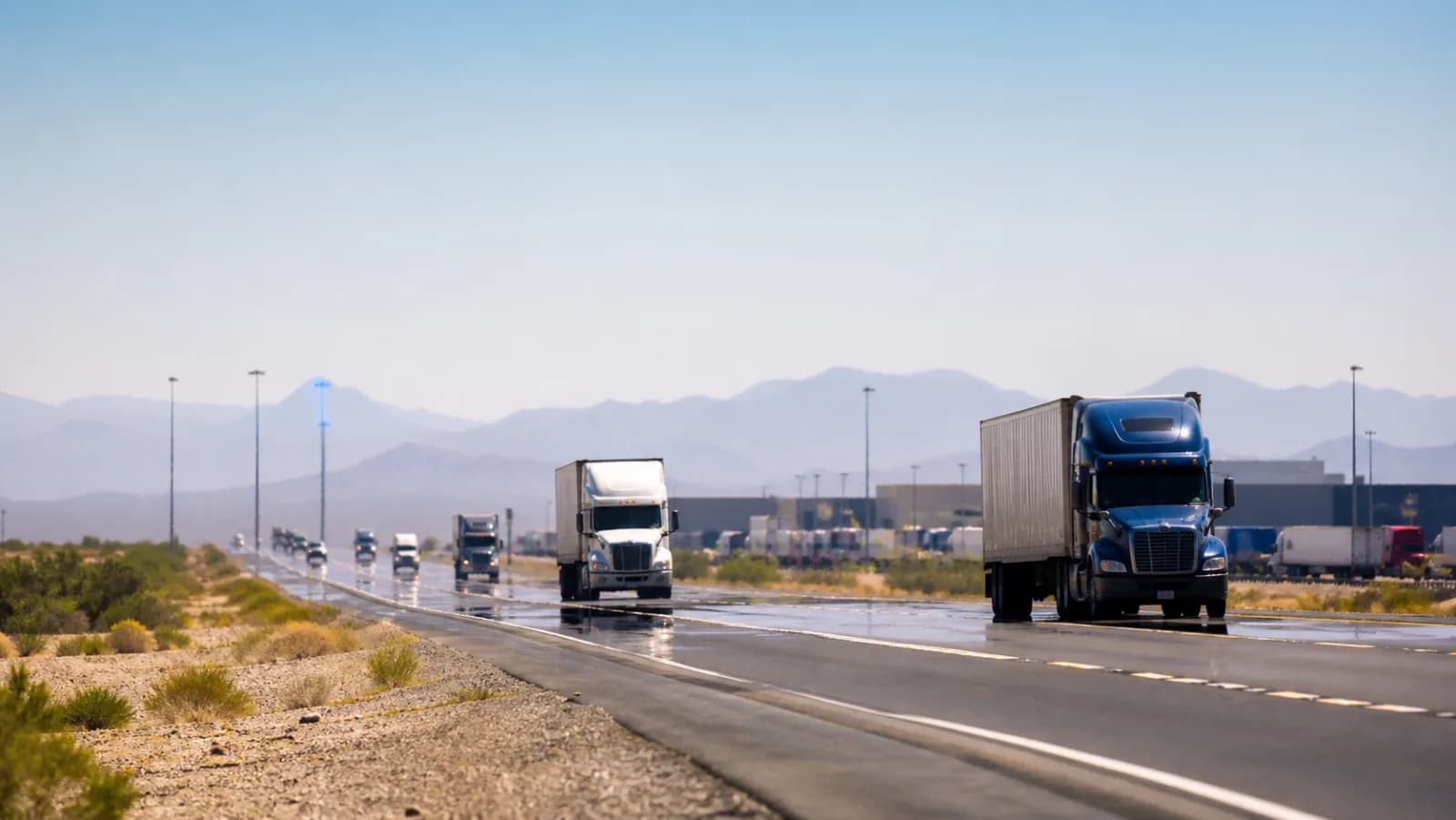 Commercial trucks traveling through a desert freight corridor with visible heat shimmer.